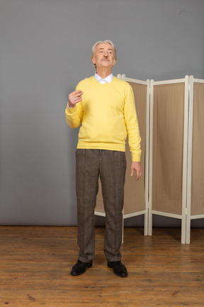 Front view of a perplexed old man raising hand while looking aside