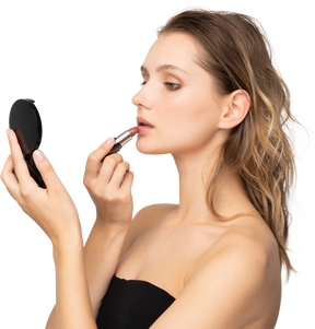 Side view of a young woman applying lipstick while holding a mirror
