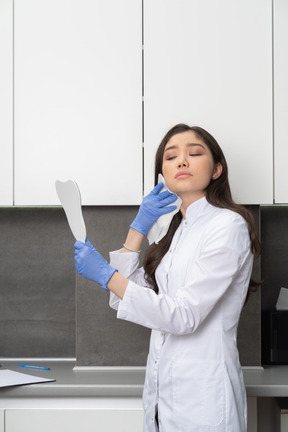 Three-quarter view of a female doctor holding a mirror and wiping her face