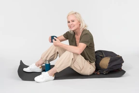 Mature female tourist sitting on tourist mat and passing on cup