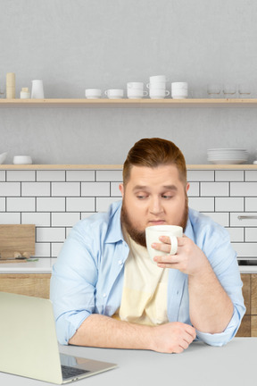A man sitting at a table drinking a cup of coffee