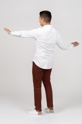 Three-quarter back view of a young latino man holding out his hands in a stopping gesture