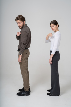 Vista lateral de um jovem casal com roupas de escritório apontando para a câmera