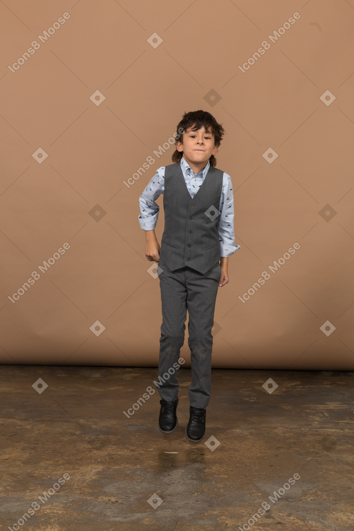 Front view of a cute boy in suit jumping