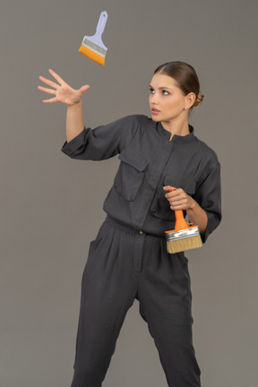 Woman in gray coveralls tossing a paint brush into the air