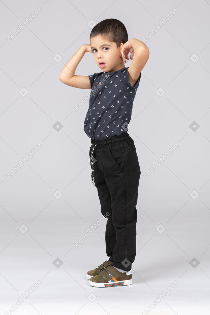 Side view of a cute boy standing with raised hands and looking at camera