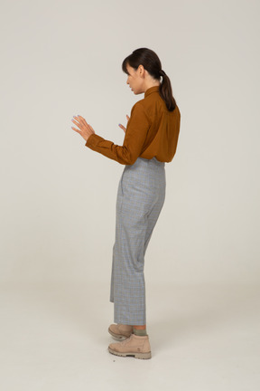 Vista posteriore di tre quarti di una giovane donna asiatica attenta in calzoni e camicetta che allunga le braccia