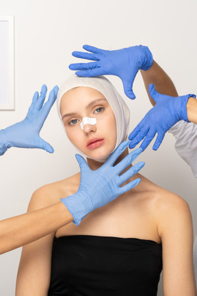 Young woman with head bandage surrounded by hands