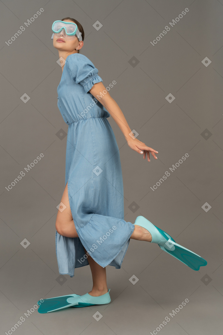 シュノーケリングマスクと足ひれで片足で立っている若い女性の側面図