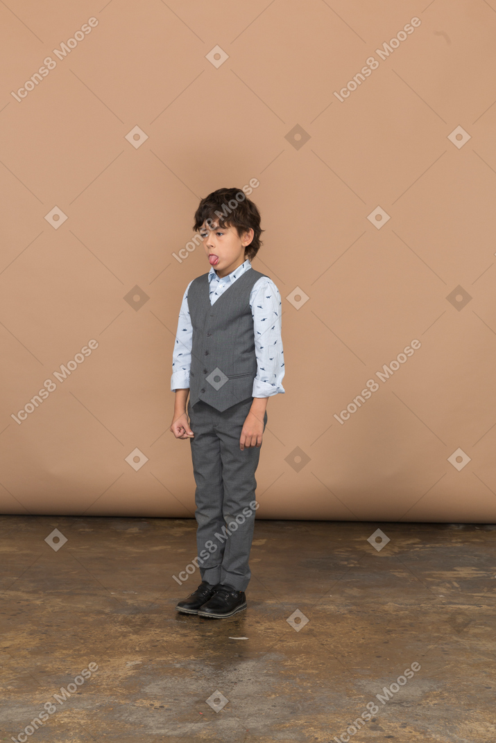 Vista frontal de um menino de terno cinza fazendo caretas