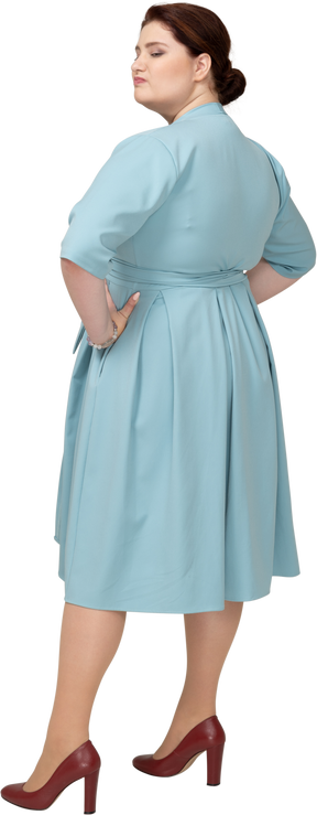 Вид сзади женщины в синем платье позирует с руками на бедрах