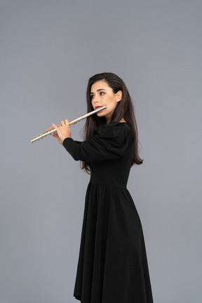 Three-quarter view of a serious young lady in black dress playing the flute