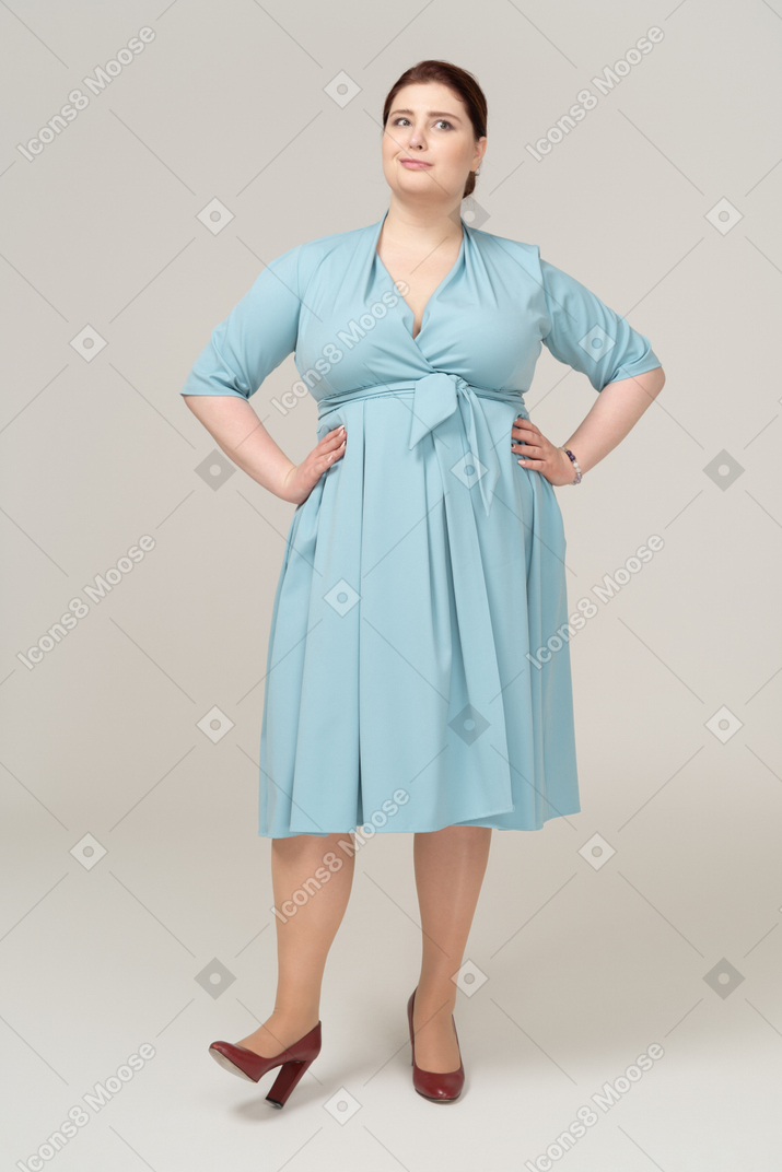 Vue de face d'une femme en robe bleue posant avec les mains sur les hanches