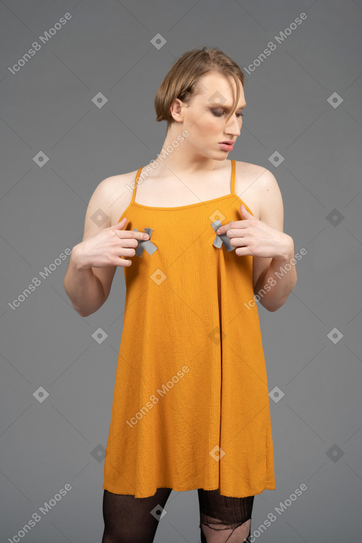 Young non-binary person in orange dress touching chest