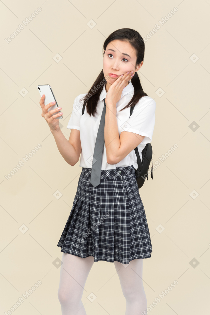 Menina asiática da escola pensativa olhando para o telefone
