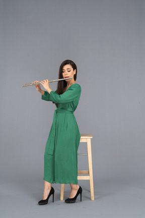 Full-length of a young lady in green dress sitting on a chair while playing the clarinet
