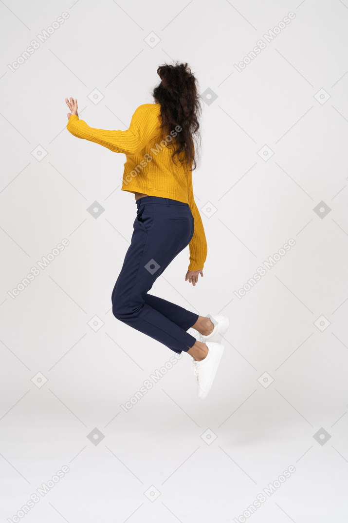 Vista lateral de una niña en ropa casual saltando y tocando su pie