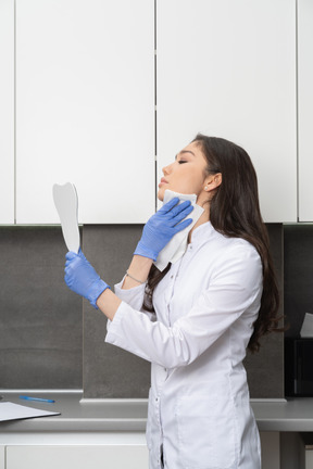 Side view of a female doctor holding a mirror and wiping her face