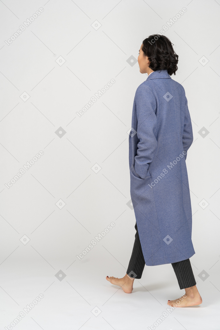 Punto di vista posteriore della giovane donna in cappotto che cammina a piedi nudi