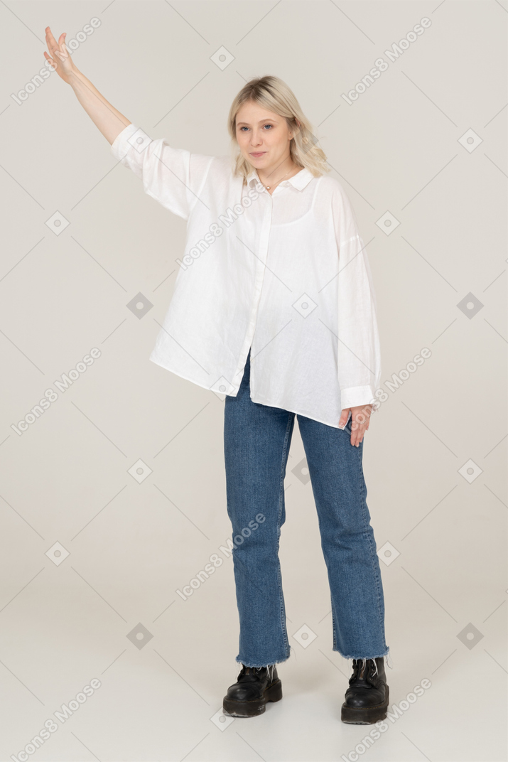 Vista frontale di una giovane donna bionda che osserva da parte e alzando la mano