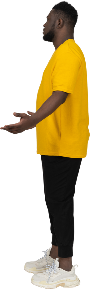 Side view of a displeased young dark-skinned man in yellow t-shirt outspreading hands