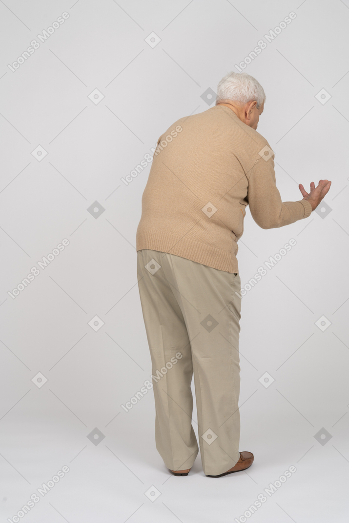 Rear view of an old man in casual clothes standing with outstretched arm and explaining something