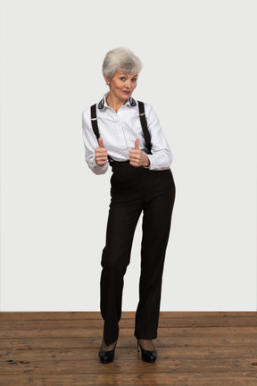 Vista frontale di una vecchia donna scontenta in abiti da ufficio che mostra un pollice in su con entrambe le mani
