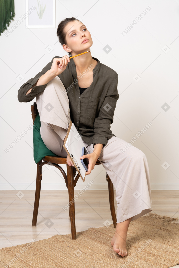 椅子に座ってメモをとる家庭服を着て思いやりのある若い女性の正面図