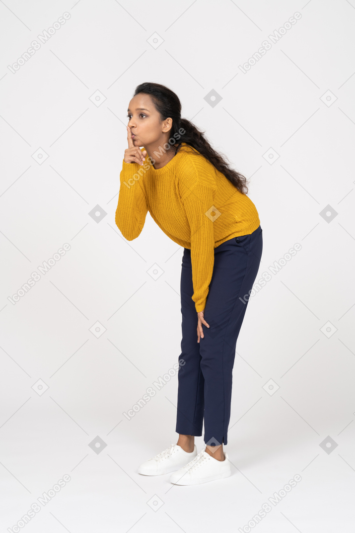 Vista lateral de uma garota com roupas casuais fazendo um gesto de shh