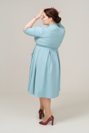 Rear view of a woman in blue dress standing with hands on head