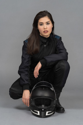 A beautiful young woman hunkering down next to a helmet