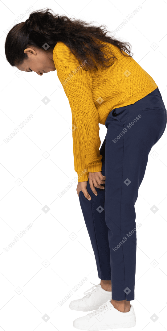 Side view of a girl in casual clothes bending down and touching hurting knee