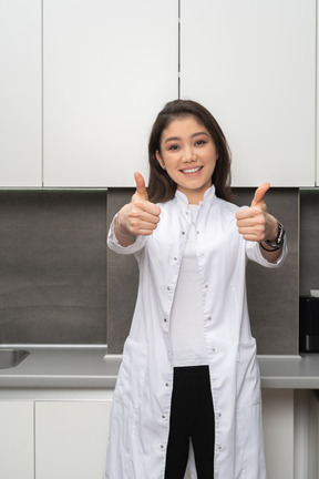 Front view of a smiling  female doctor showing a like gesture with both her hands