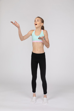 Front view of a surprised teen girl in sportswear raising hands and opening her mouth