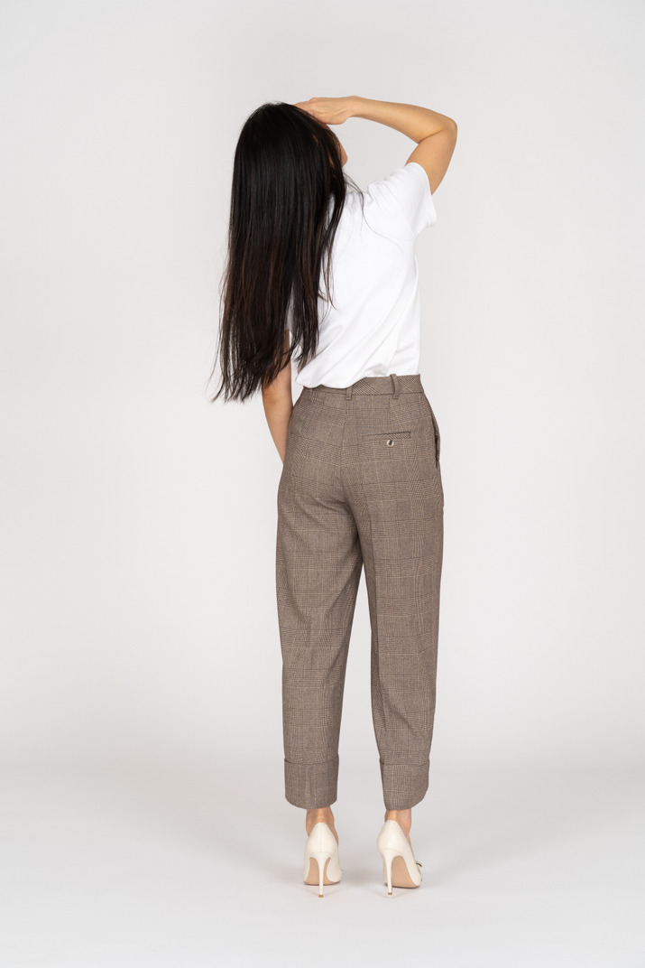 Back view of a young lady in breeches and t-shirt raising hear hand while looking up