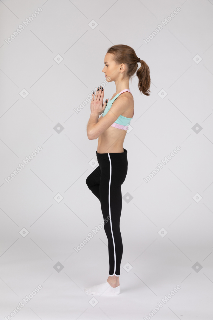 一个女孩在一条腿上保持平衡，手牵着手的运动服的侧视图