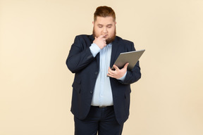 Pensive young overweight office worker holding digital tablet