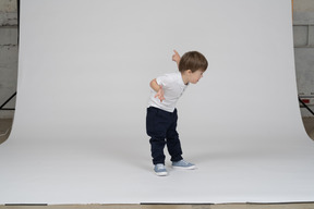 Three-quarter view of a boy leaning forward and pointing behind his back quizzically