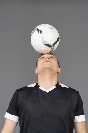 彼の頭にボールを保持している男性のサッカー選手の正面図