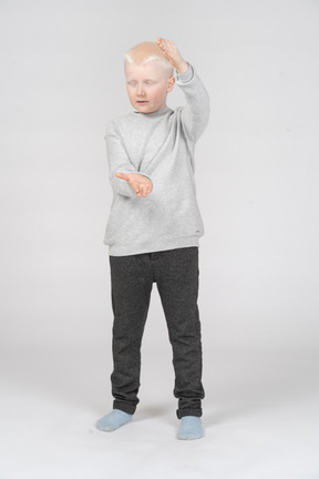 Boy with closed eyes showing the size of something with his hands