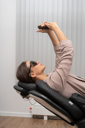 Une patiente dans la chaise de dentiste prenant un selfie dans des lunettes médicales