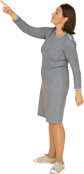 Vista lateral de una mujer en vestido gris apuntando hacia arriba con un dedo