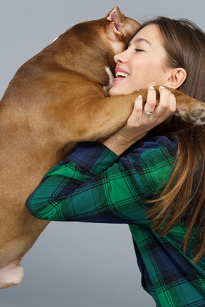 Vista laterale di una donna sorridente in camicia a quadri che abbraccia il suo bulldog