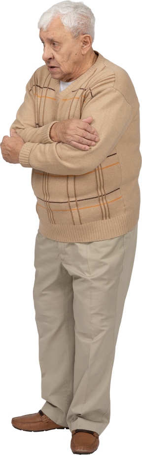 Front view of a scared old man in casual clothes hugging himself