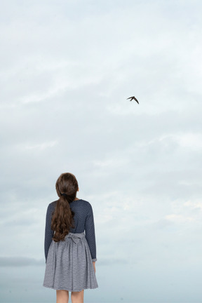 A girl is standing on a beach looking at a bird