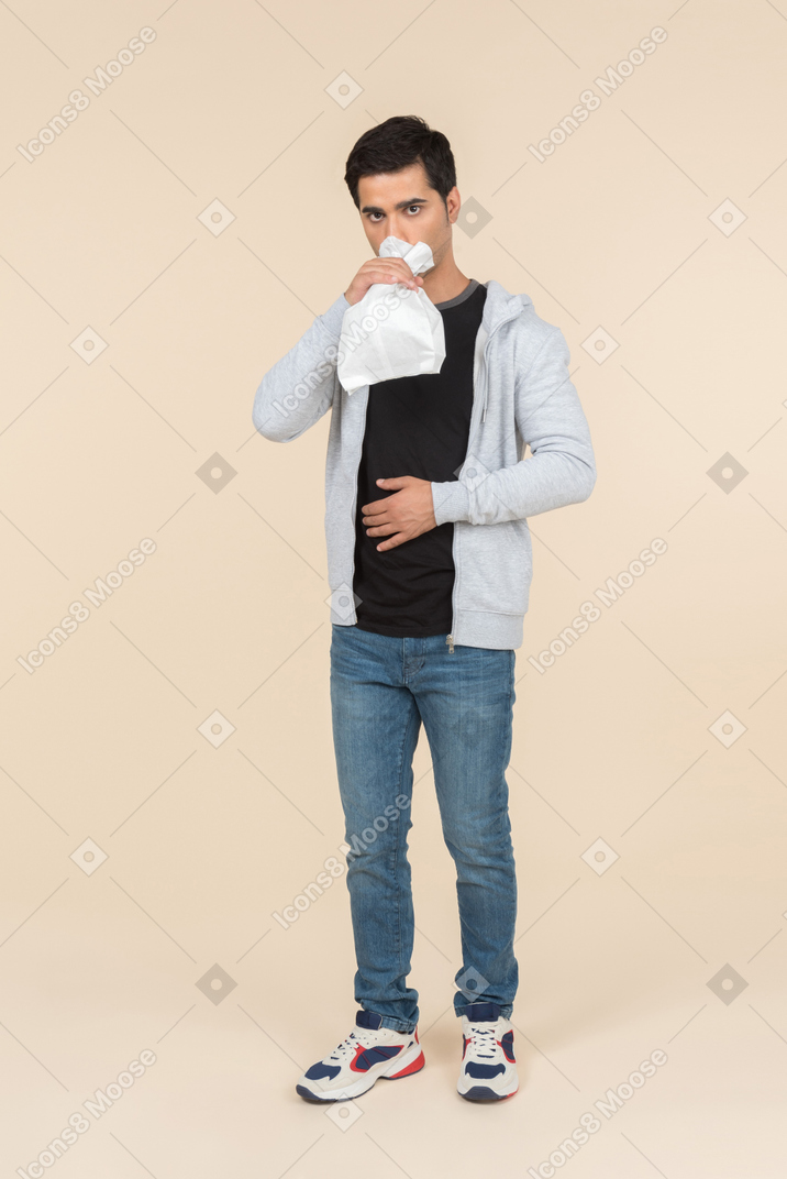 Молодой кавказский человек дышит в бумажный пакет
