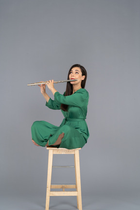 De cuerpo entero de una señorita tocando el clarinete sentada con las piernas cruzadas en una silla de madera