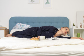 Vista frontal de uma jovem deitada na cama tomando café da manhã