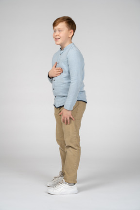 Vista lateral de um menino bonito posando com a mão no peito