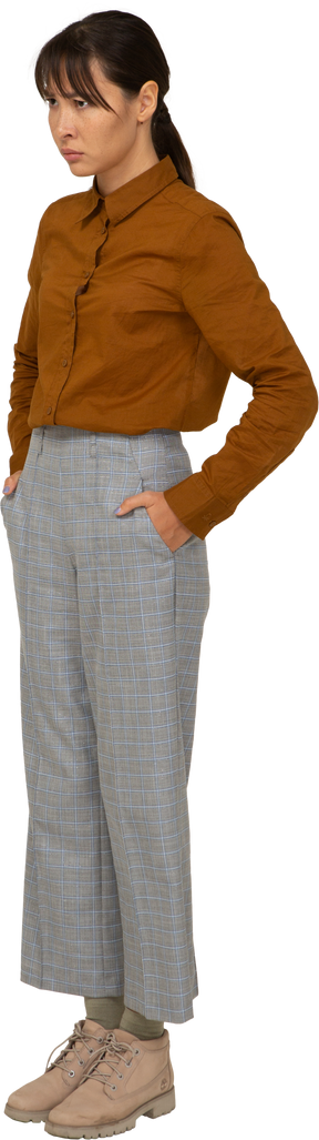 Vista de três quartos de uma jovem mulher asiática de calça e blusa, colocando as mãos nos bolsos